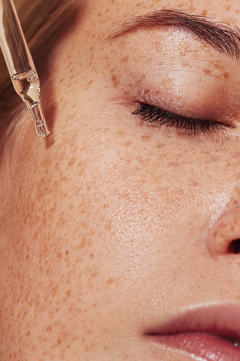 Frau mit geschlossenen Augen tropft Serum aufs Gesicht