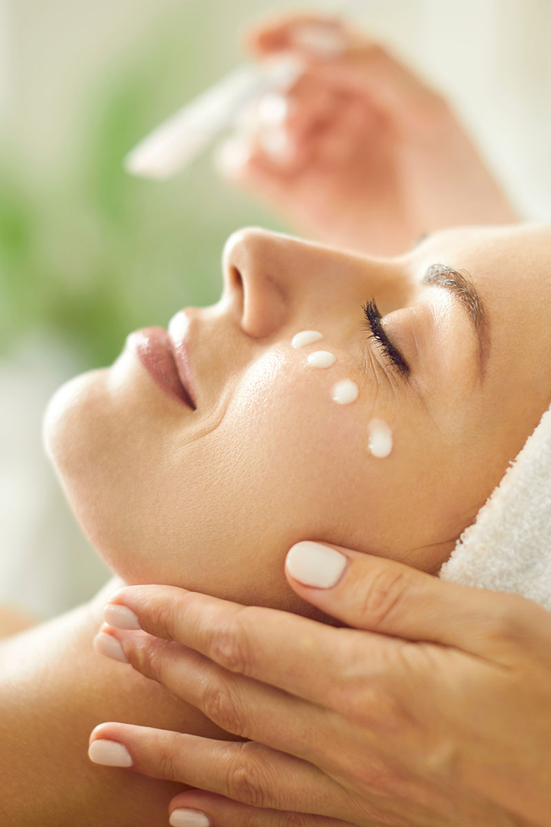 Frau mit geschlossenen Augen und Cremetupfern auf ihren Wangen