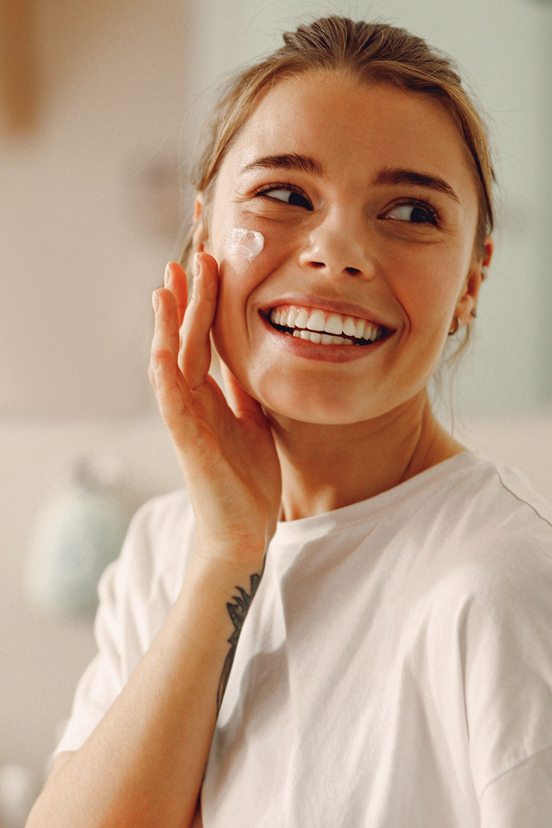Lächelnde Frau mit Gesichtscreme im Gesicht auf hellem Hintergrund