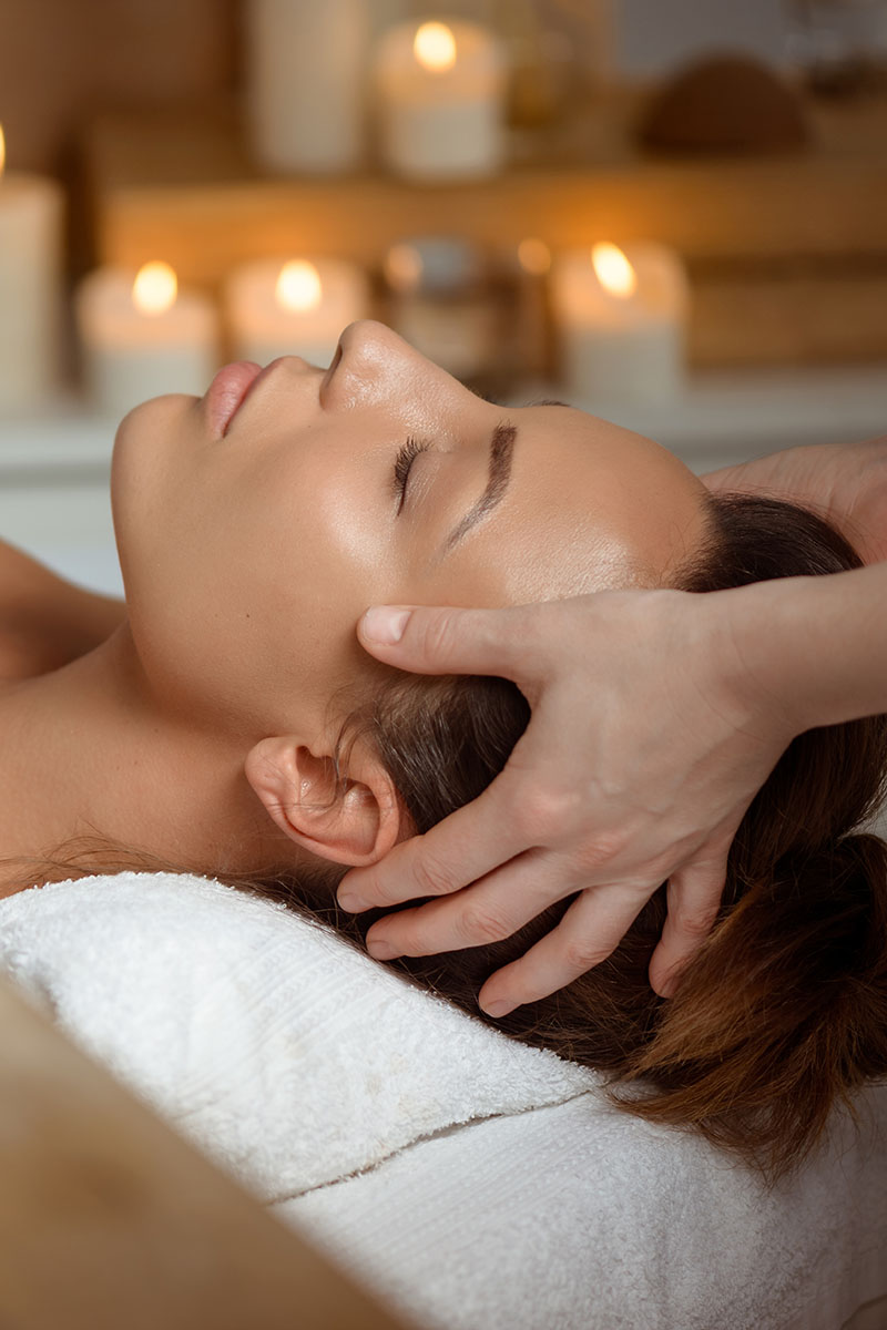 Kopfmassage bei einer Frau, Kerzenschein im Hintergrund