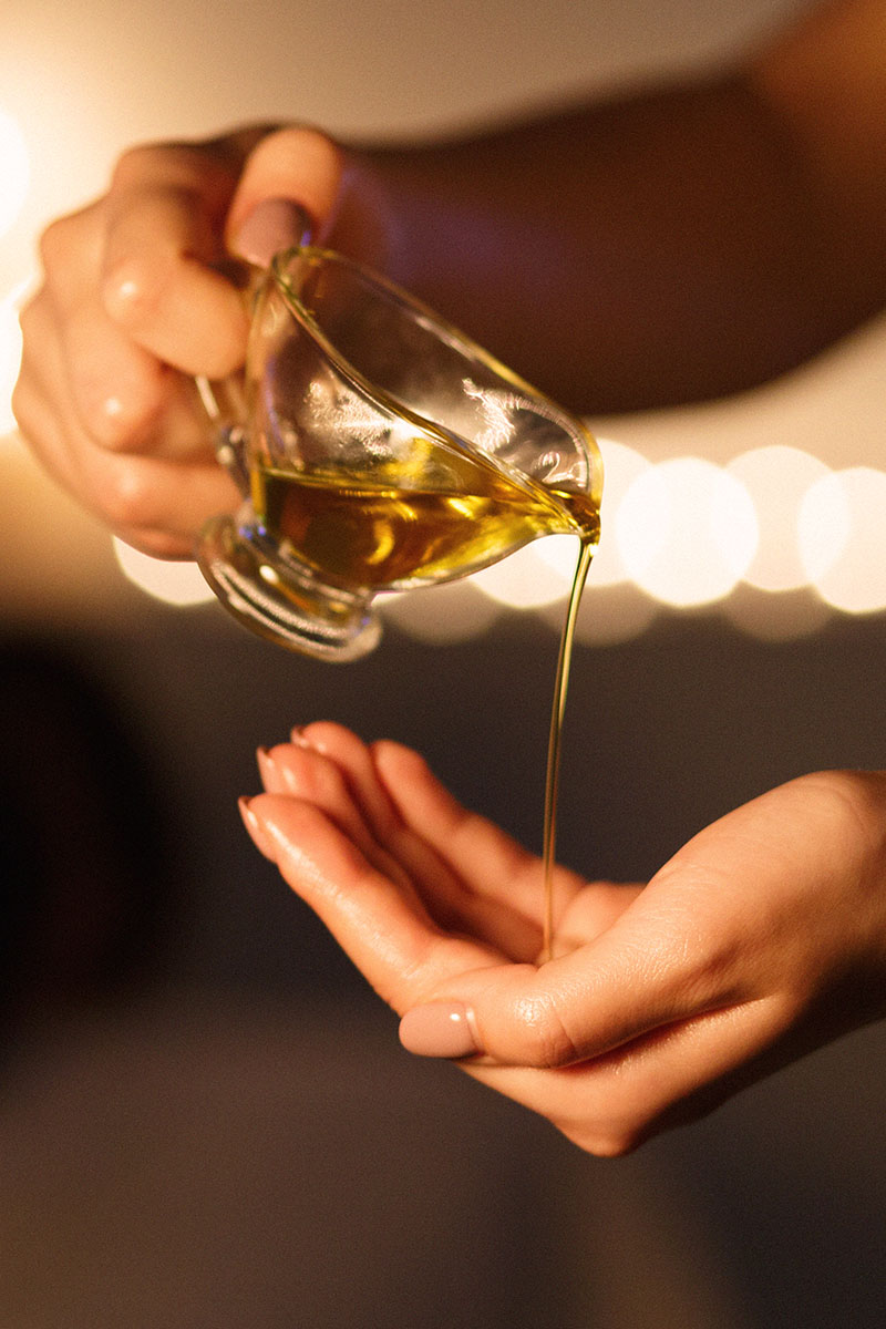 Massageöl wird über Hand gegossen, vor dunklem Hintergrund mit Kerzenlicht